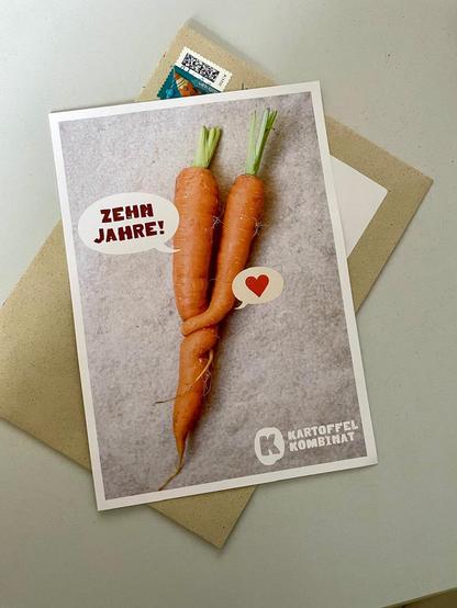 Grußkarte mit einem Foto zweier ineinander verdreht gewachsener Karotten, einrm Herz und dem Text "10 Jahre" sowie dem Logo des Kartoffelkombinats.